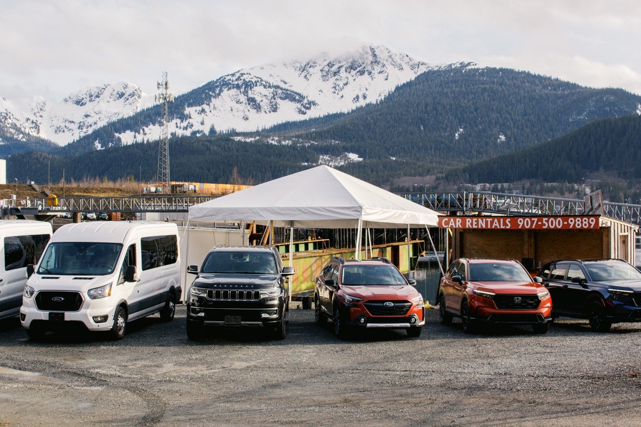 Explore Juneau rental lot on Thane Road with vans and SUVs beneath snow-capped mountains